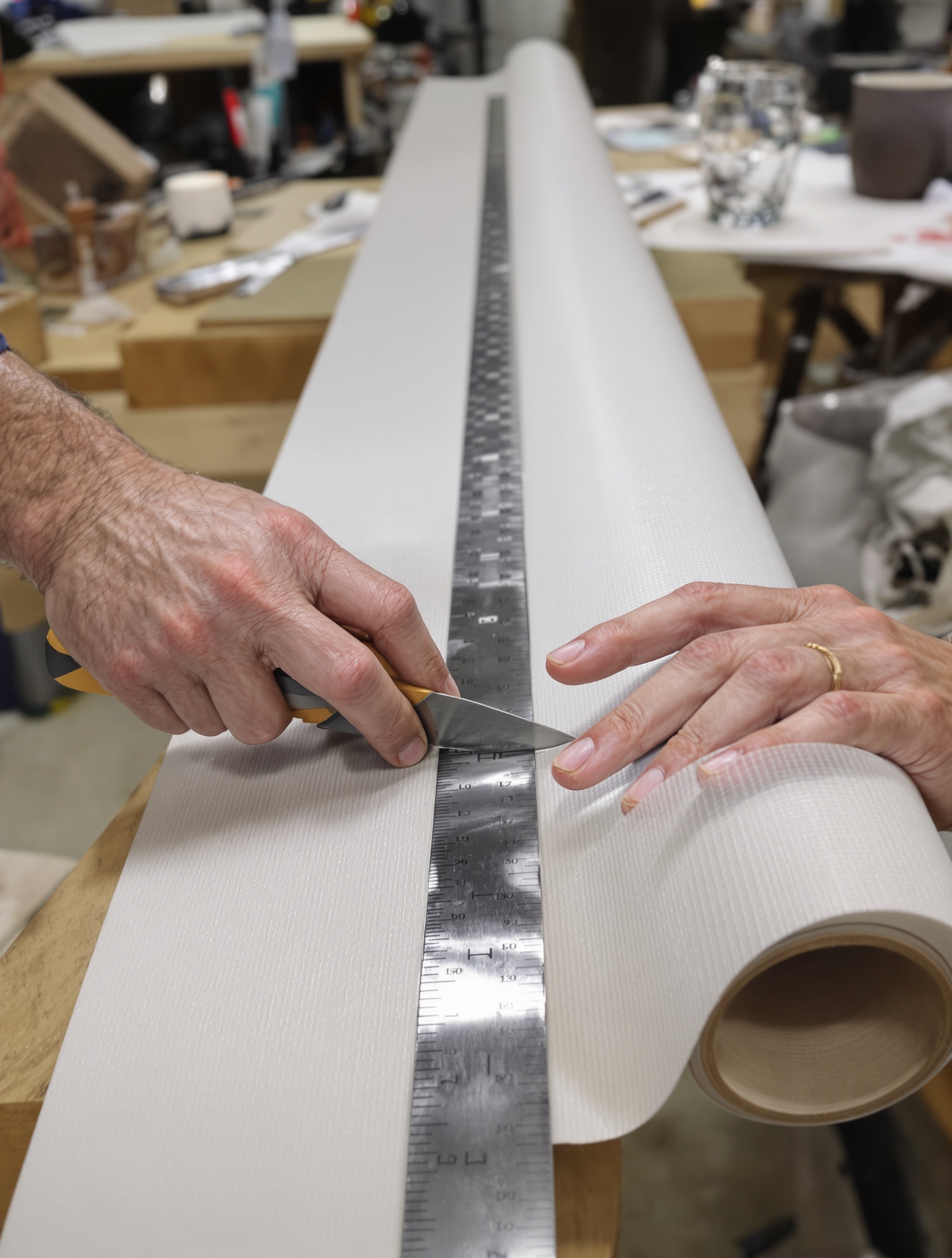 Un artisan coupant un lé de fibre de verre à l'aide d'un cutter et d'une règle métallique, posé sur le rouleau, illustrant la précision nécessaire pour les découpes.