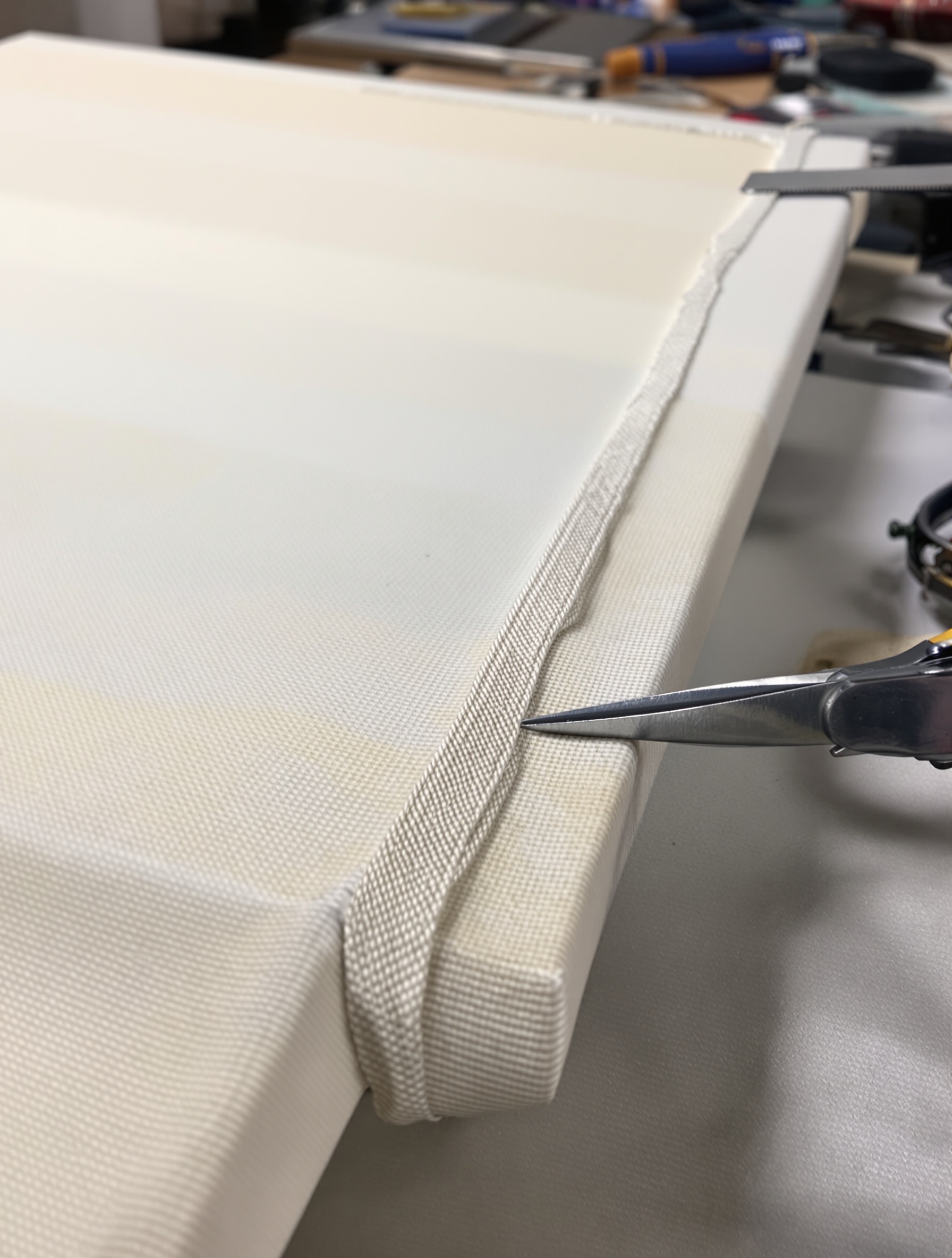 Pose d’un galon de finition aligné sur une toile tendue avec outils de précision.